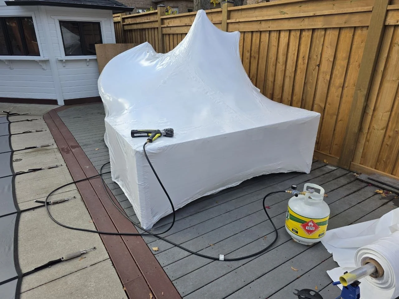Custom-shaped patio furniture shrink wrap installation with tools and propane equipment