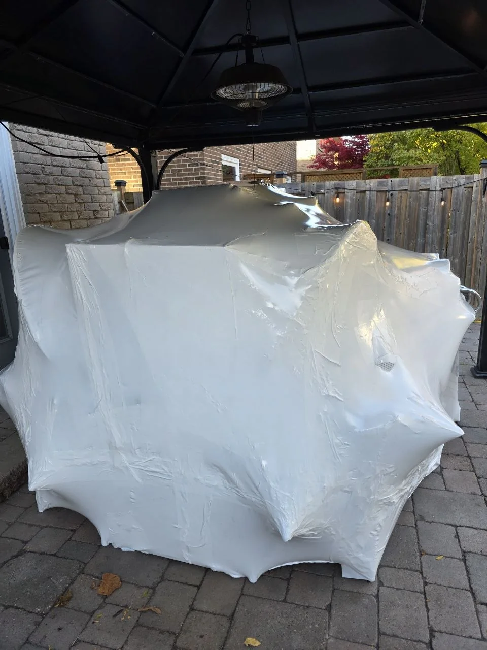 Backyard items grouped and covered with white shrink wrap